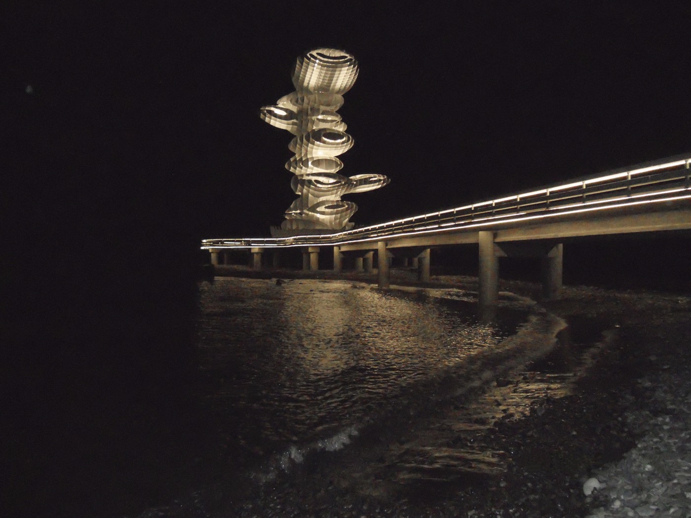 Lazika Pier Sculpture Georgien Anaklia, Nachtansicht mit leuchtender Skulptur und Pierbeleuchtung und dunklem Meer